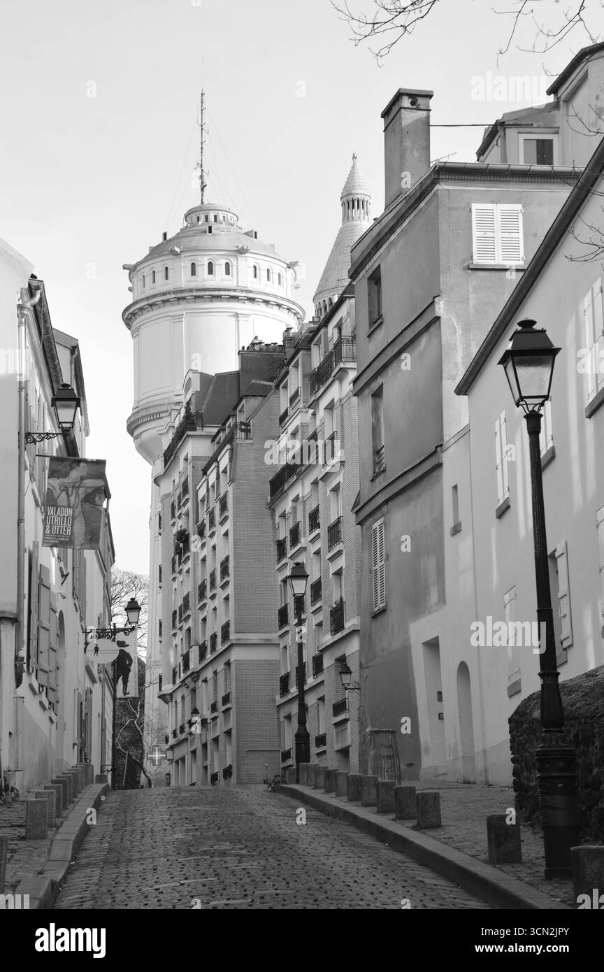 Historische Kopfsteinpflasterstraße mit alten Gebäuden und Wasserturm in Montmartre, Paris, Frankreich, Januar, schwarz-weiß. Stockfoto