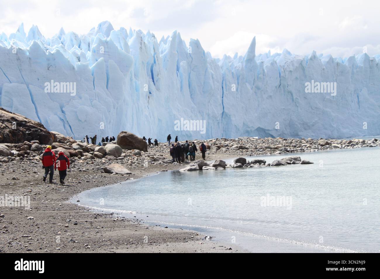 Touristen wandern entlang der felsigen Küste in der Nähe des Perito Moreno Gletschers, Patagonien, Argentinien. Majestätische blaue Eiswand, die sich über dem Lago Argentino erhebt. Stockfoto