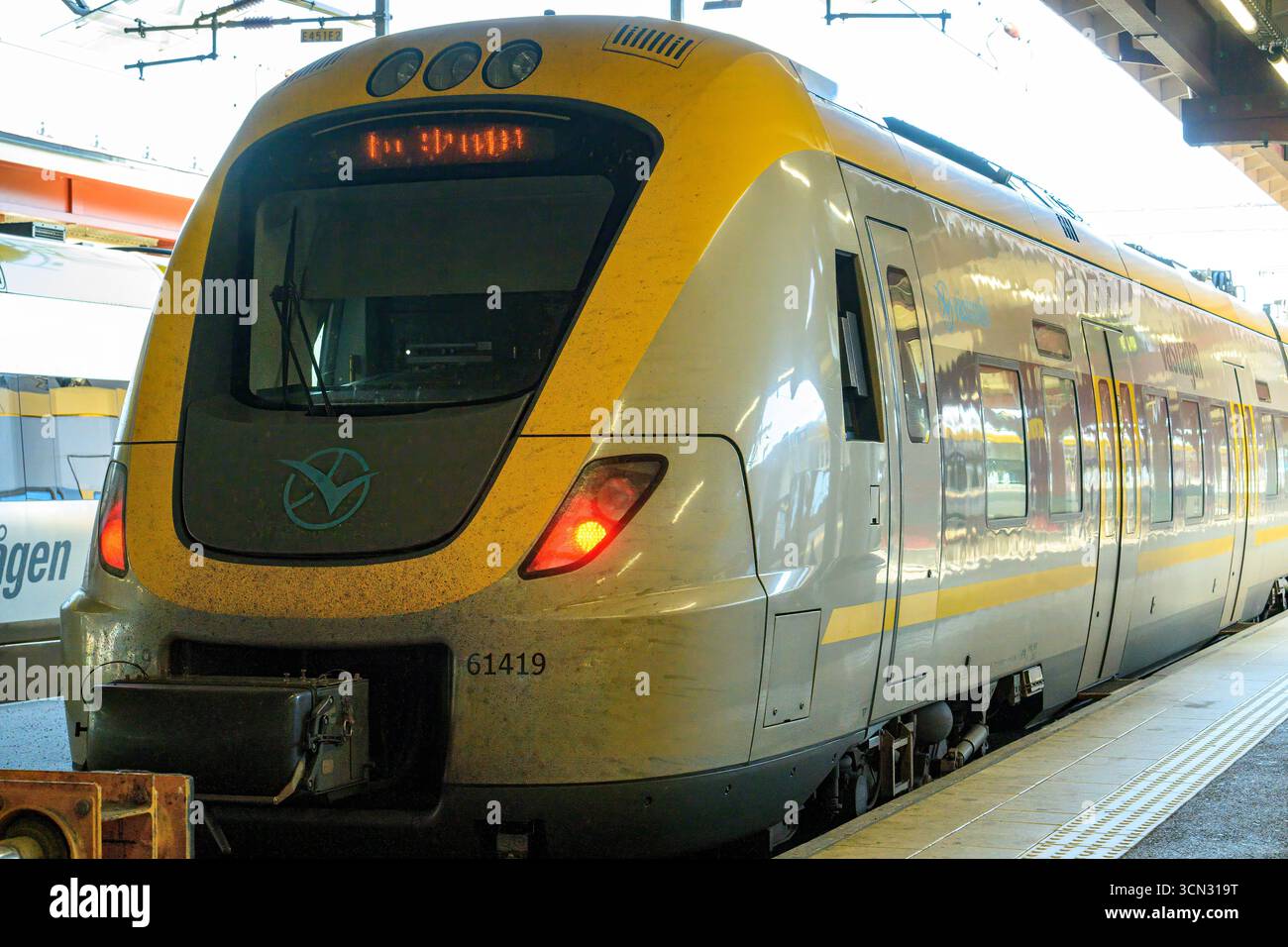 Ein moderner Zug fährt an einem sonnigen Tag in einen belebten Bahnhof. Reisende erwarten sehnsüchtig, an Bord zu gehen, während andere von Bord gehen und eine lebhafte Szene im t schaffen Stockfoto