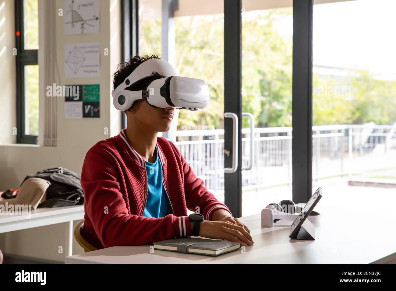 Männlicher Teenager, der ein Virtual-Reality-Headset trägt, erkundet mathematische Diagramme auf einem Tablet am modernen Schreibtisch Stockfoto