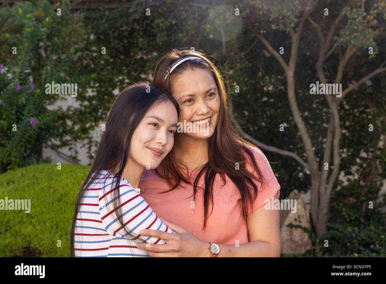 Asiatische Mutter und Tochter umarmen sich im Garten, während sie Armbanduhr und Stirnband tragen Stockfoto