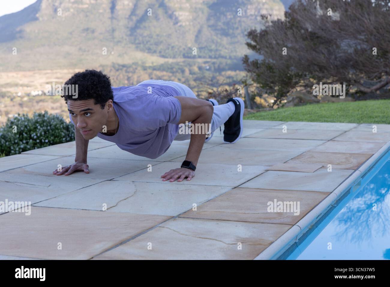 afroamerikanischer Mann, der Liegestütze auf der Terrasse neben dem Pool in Laufschuhen-Fitness-Tracker durchführt Stockfoto