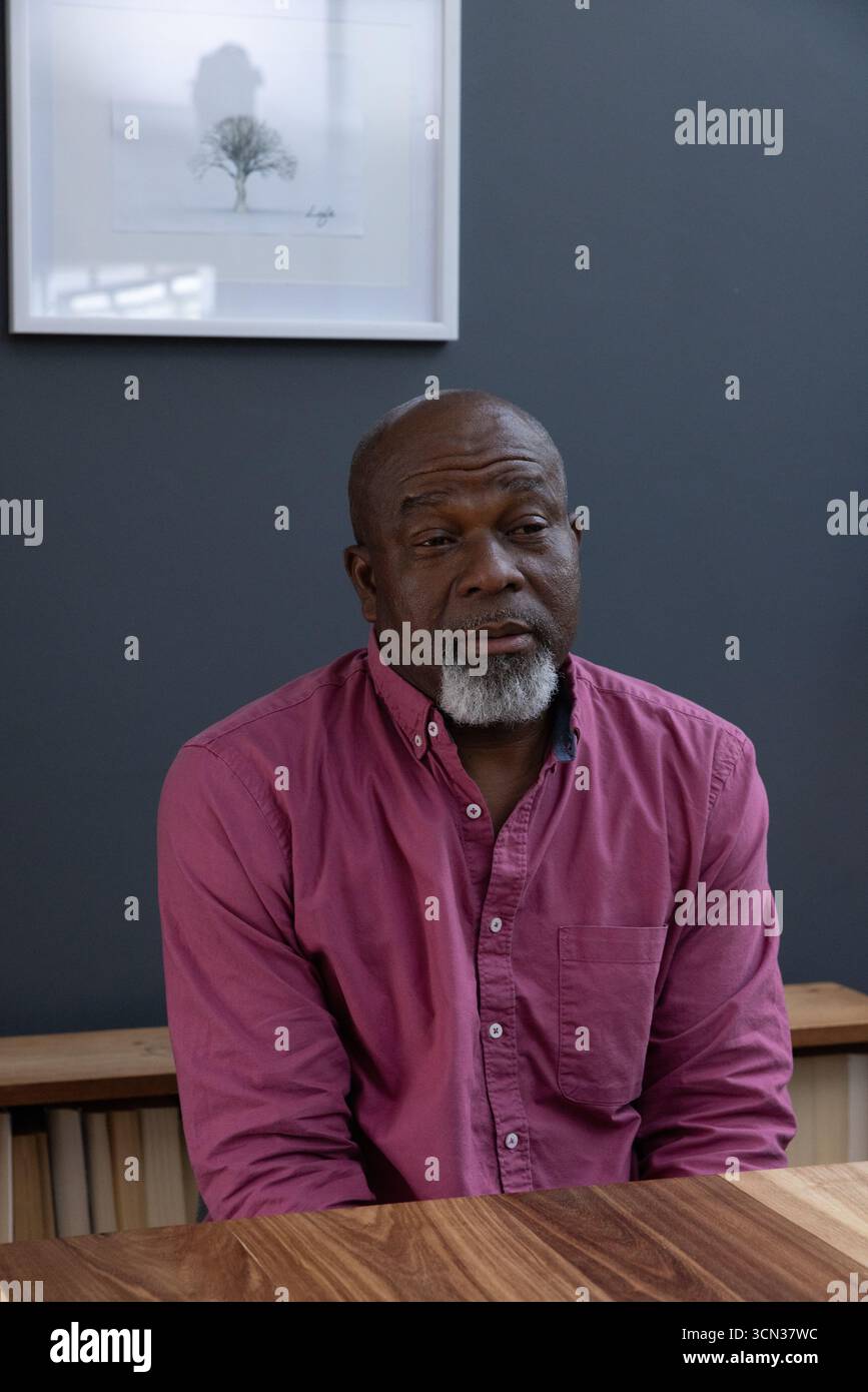 Ranghoher afroamerikaner reflektiert, während er im Arbeitszimmer am Tisch unter Baumabdruck sitzt Stockfoto