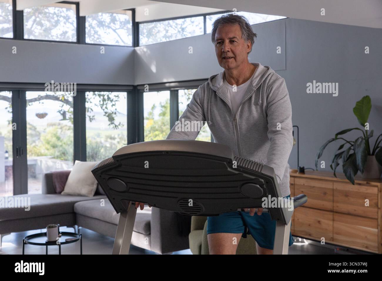 Mann, der auf dem Laufband im Wohnzimmer mit Sofa und Kaffeetasse trainiert, Kopierraum Stockfoto