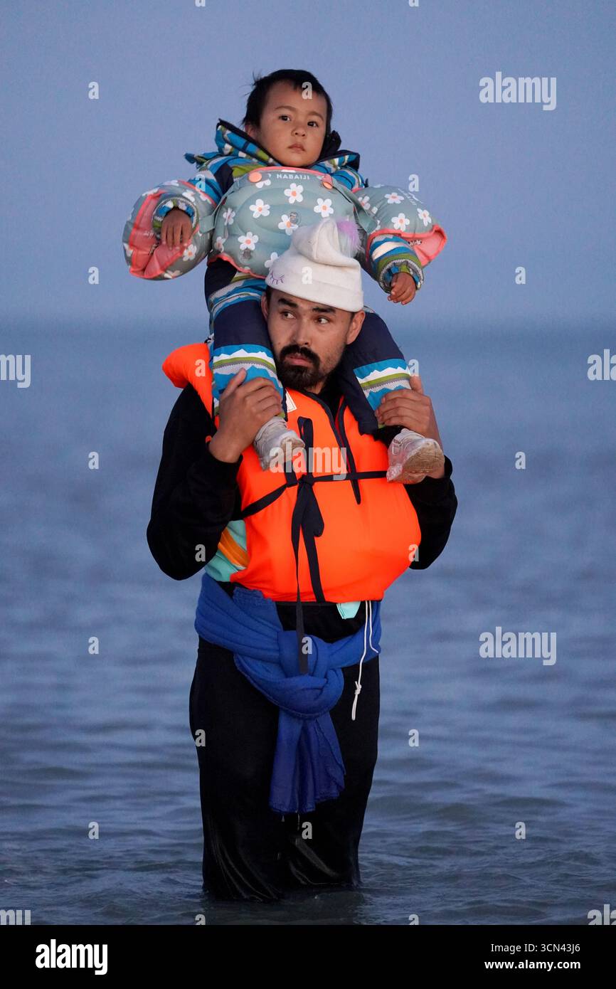 Eine Person, die ein Kind mit sich trägt, das als Migranten gilt, waten in der Nähe von Gravelines in Frankreich ins Meer. Bilddatum: Freitag, 19. September 2025. Stockfoto