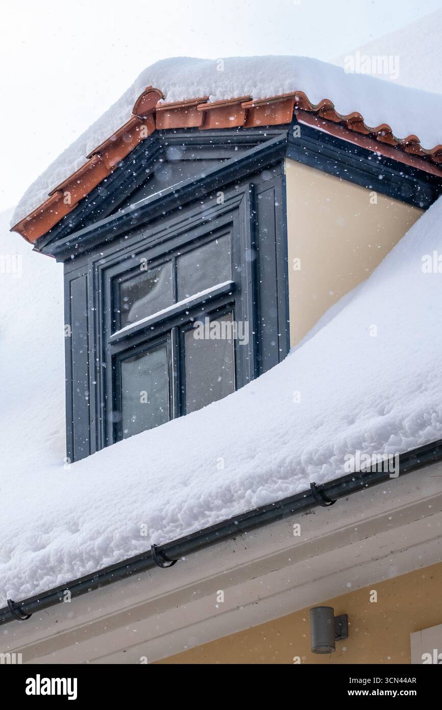 Terrakotta-Dachziegel zieren ein schneebedecktes Haus mit Dachfenstern, die traditionelle Konstruktion und langlebige Materialien im Winter hervorheben Stockfoto