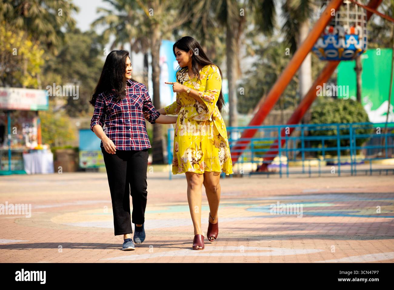 Zwei Frauen, die im Vergnügungspark spazieren gehen und sprechen - freundlicher Outdoor-Moment Stockfoto