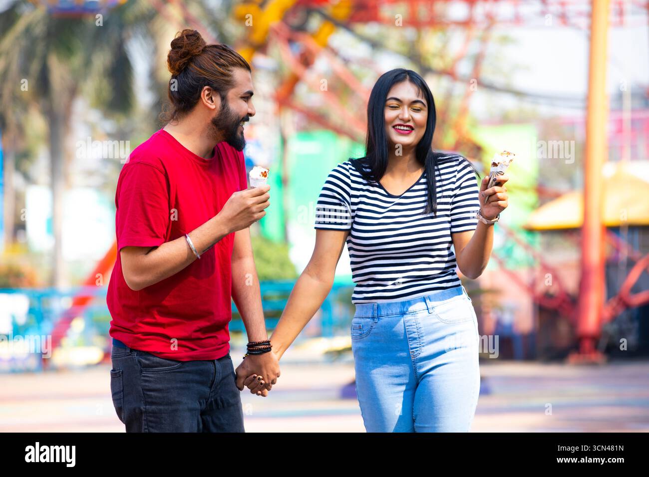 Ein Paar genießt Eis und hält Hände - ein verspielter Vergnügungspark-Moment Stockfoto