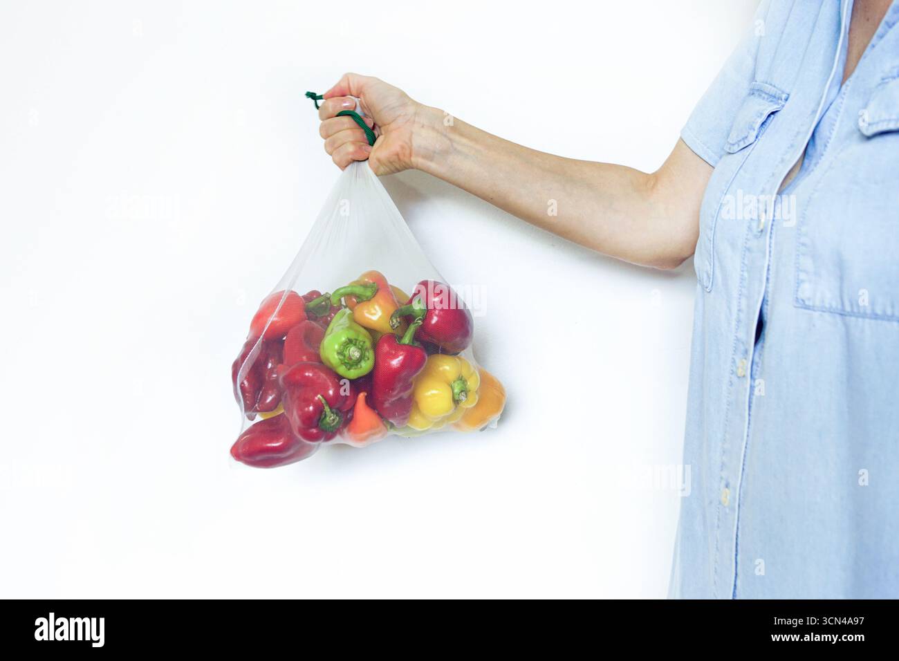 Umweltfreundliche Netztasche mit Paprika, die von Hand auf weißem Hintergrund getragen werden. Symbol für Plastikfreikäufe, verantwortungsbewussten Konsum, pflanzliche Ernährung Stockfoto