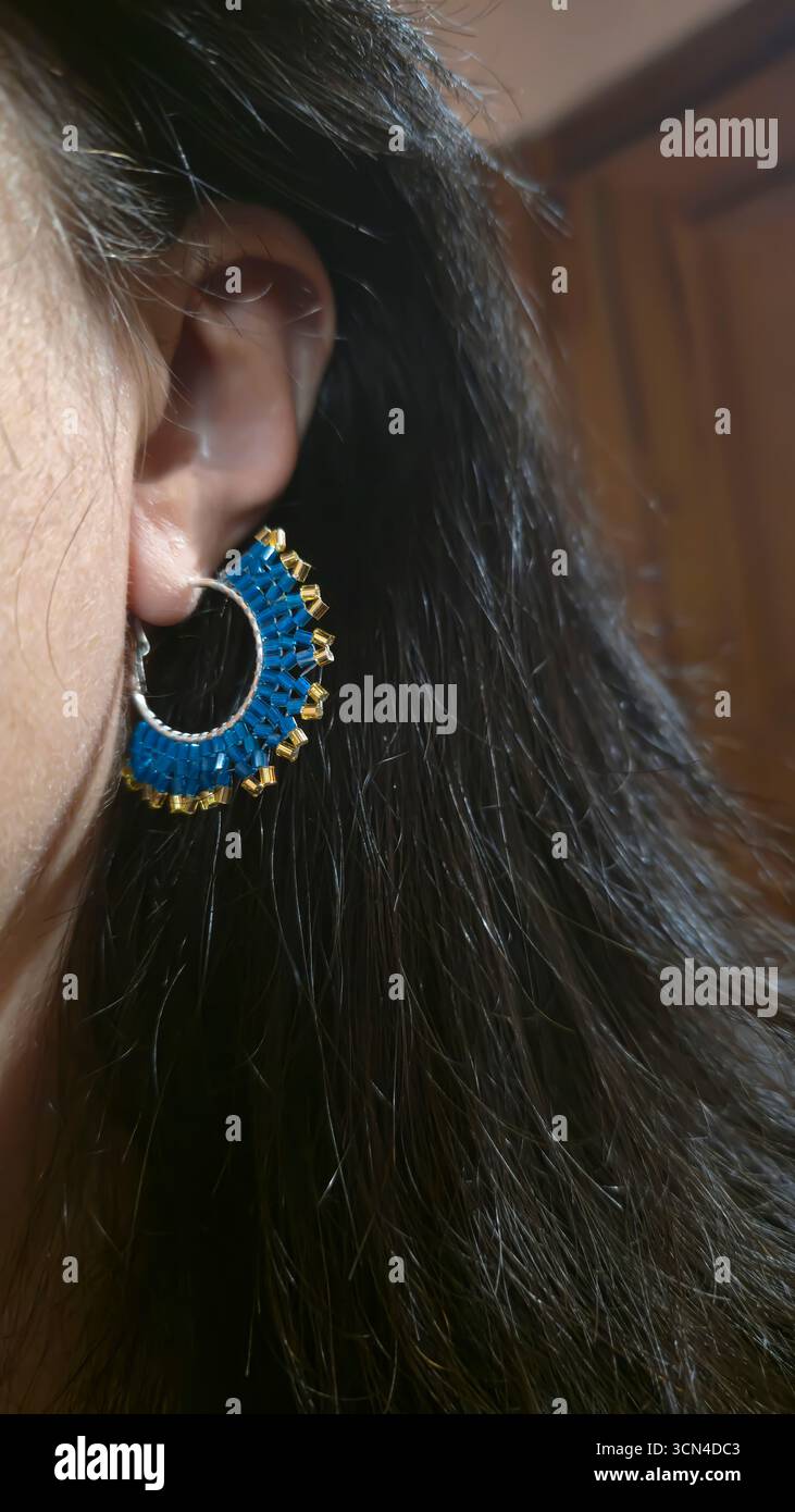 Handgefertigte Perlen- und Ohrringe am Ohr eines Mädchens. Produktvorführung. Modetrends. Stockfoto