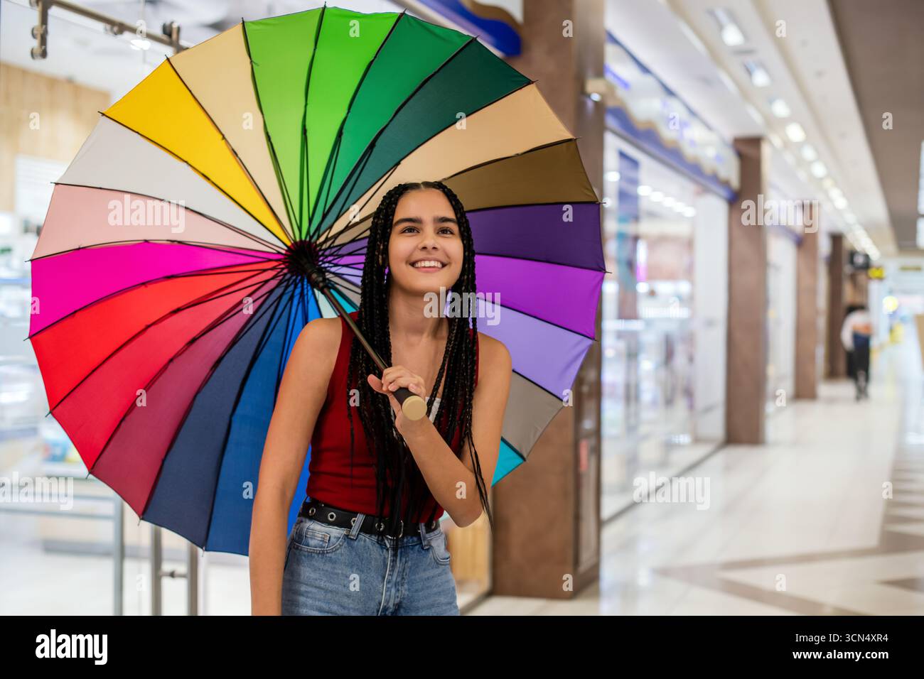 Mädchen mit Zöpfen hält Regenbogenschirm im Einkaufszentrum. Stockfoto