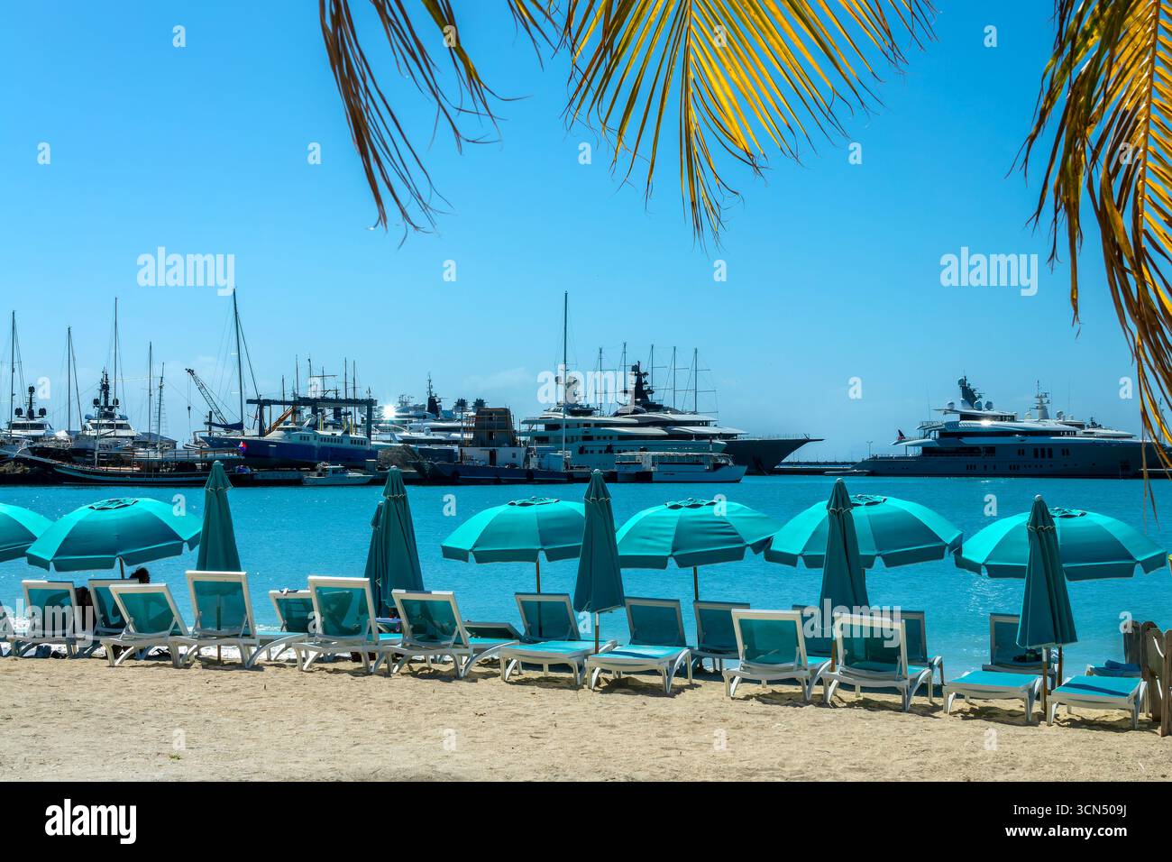 Stühle und Sonnenschirme am Great Bay Beach mit Booten im Yachthafen von Philipsburg, karibische Landschaft, Insel St. Maarten (St. Martin), niederländische Westindien Stockfoto