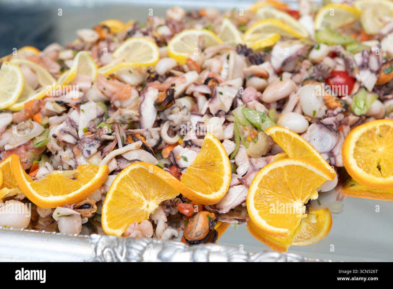 Frischer Salat mit Meeresfrüchten, gewürzt mit Zitronen- und Orangenscheiben, ergibt ein farbenfrohes und appetitliches Gericht Stockfoto