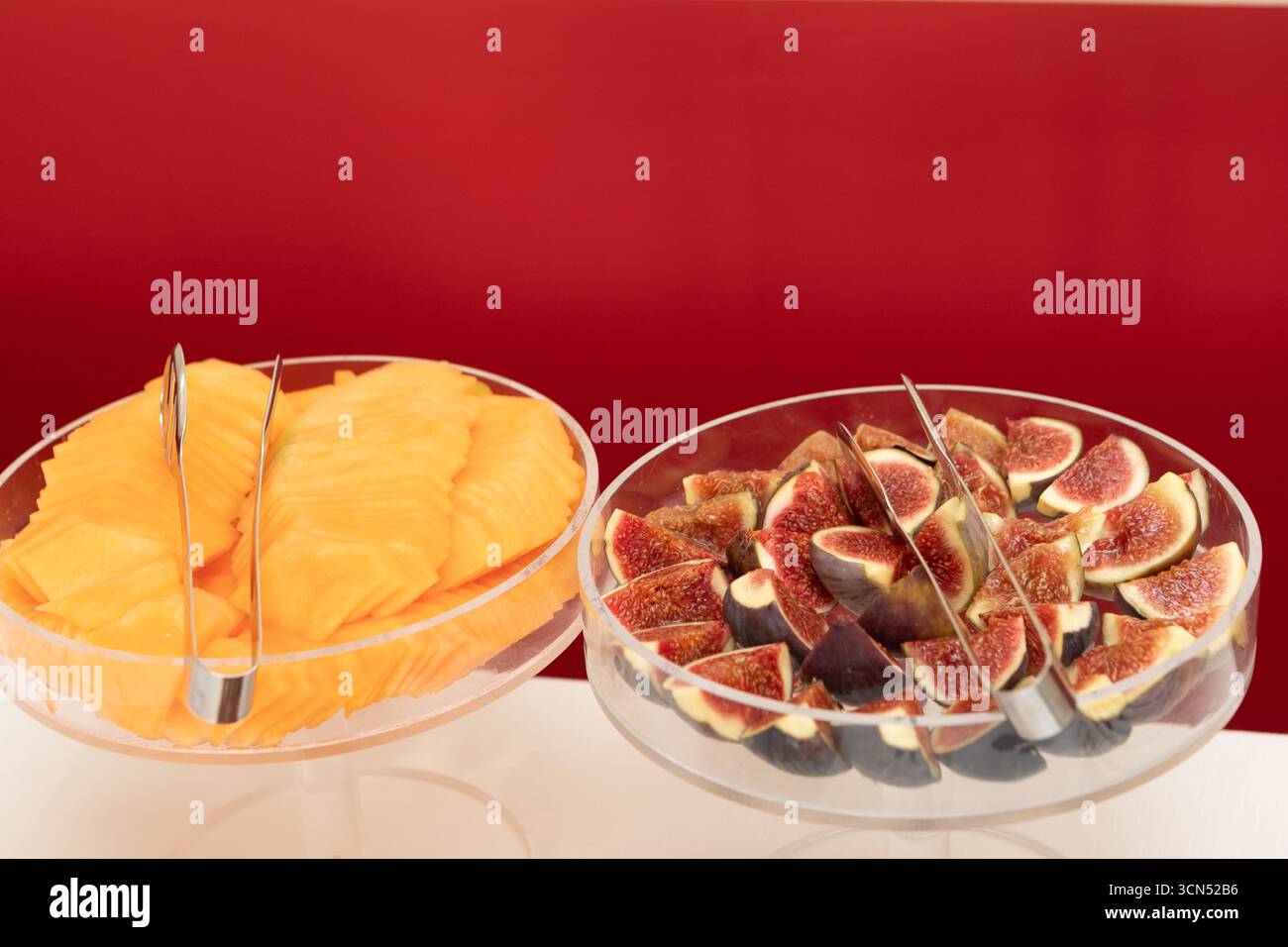 Feigen und Cantaloupe werden in Glasschüsseln mit Zange auf einem Buffet serviert Stockfoto