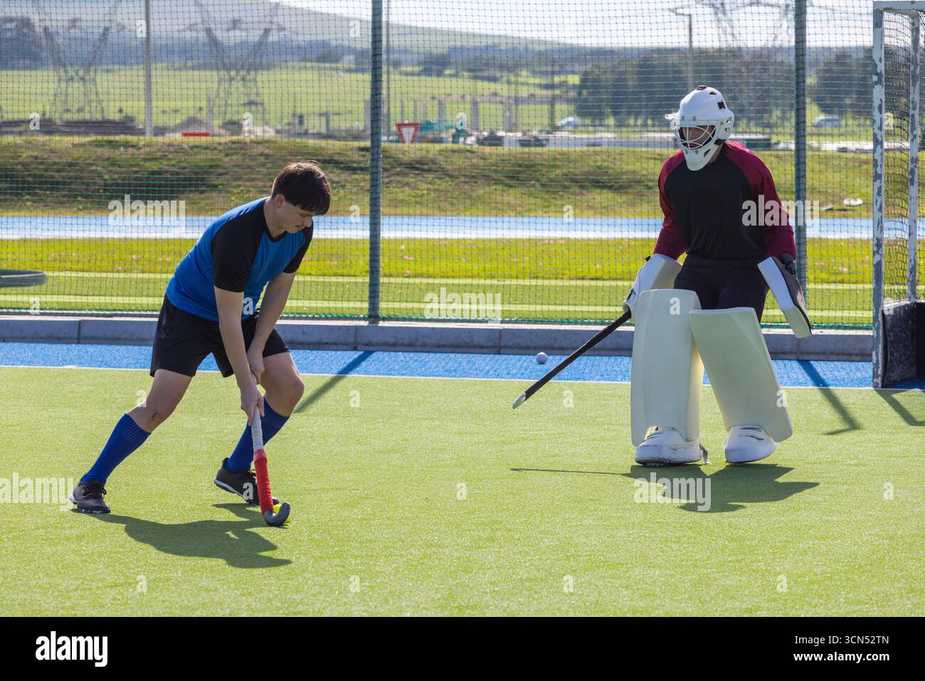 Männliche Athleten, die mit Feldhockeyschlägern am Torwart vorbeischießen Stockfoto