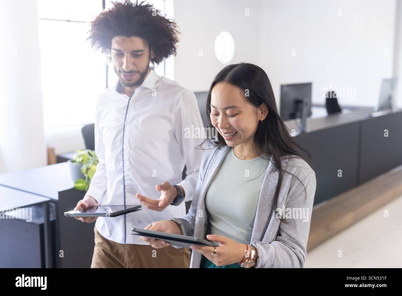 Verschiedene Kollegen stehen in der Lobby des Büros und prüfen digitale Tablets an der Rezeption und Monitoren Stockfoto