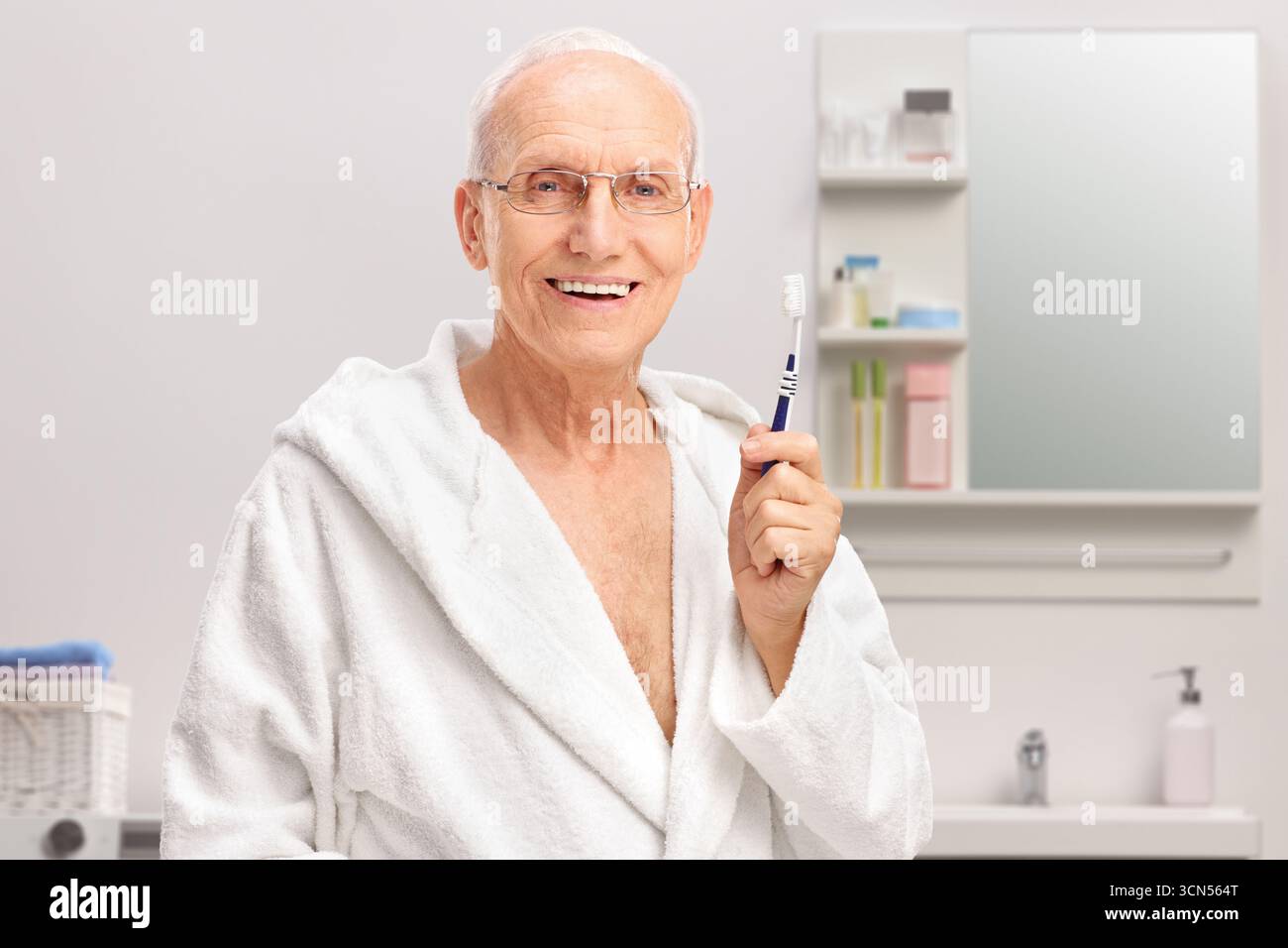 Seniorenmann im Bademantel, der eine Zahnbürste im Badezimmer hält Stockfoto