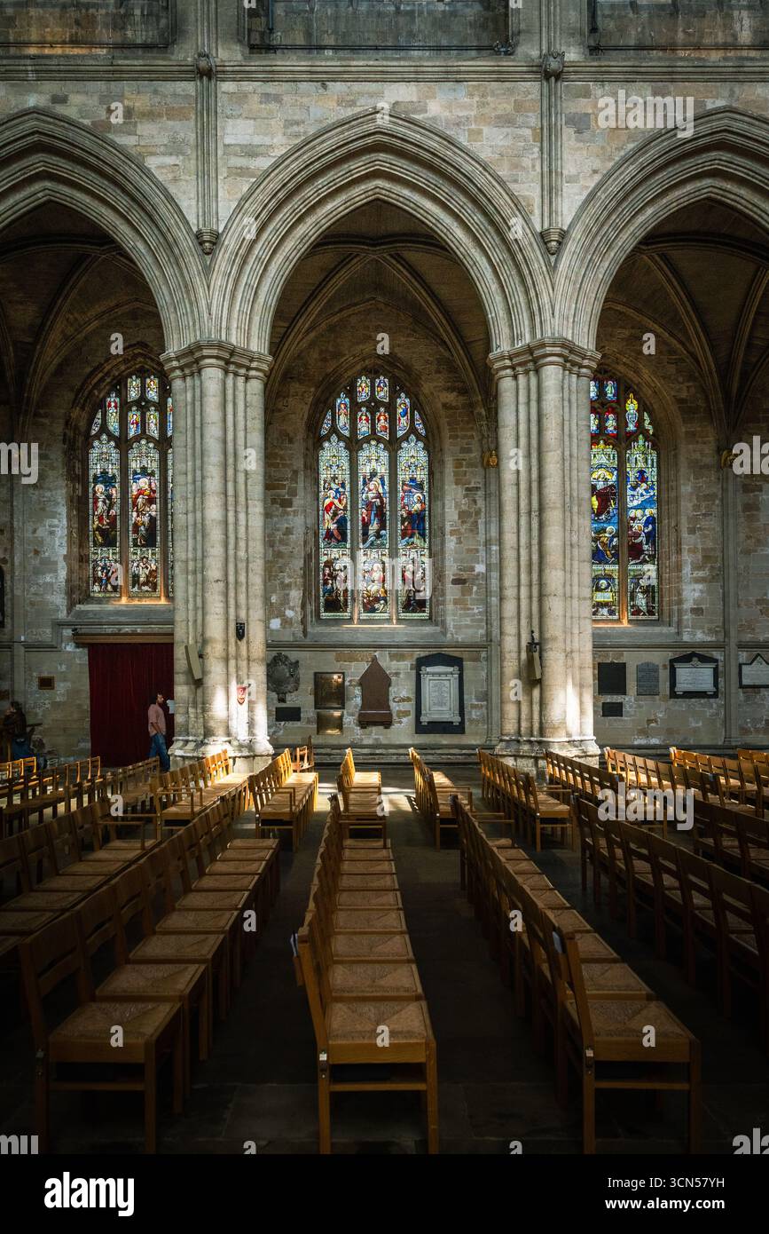Das Innere der Ripon Cathedral in North Yorkshire mit gotischen Bögen, Buntglasfenstern, Steinsäulen und Holzsitzen in der historischen Kirche Stockfoto