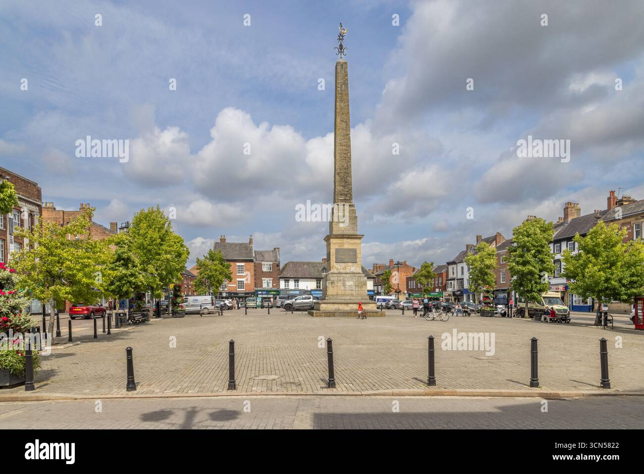 Der Ripon Obelisk auf dem Marktplatz in North Yorkshire, ein denkmalgeschütztes Denkmal aus dem Jahr 1702, das auf einem gepflasterten öffentlichen Raum mit Geschäften zu sehen ist Stockfoto