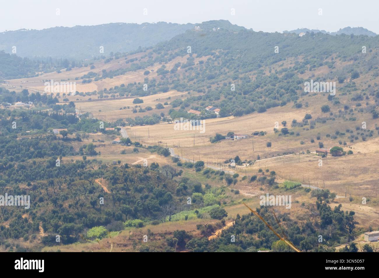 Malerischer Blick auf eine gewundene Straße durch trockene Felder und Hügel in der Nähe von sao pedro, setubal, portugal, an einem trüben Sommertag Stockfoto