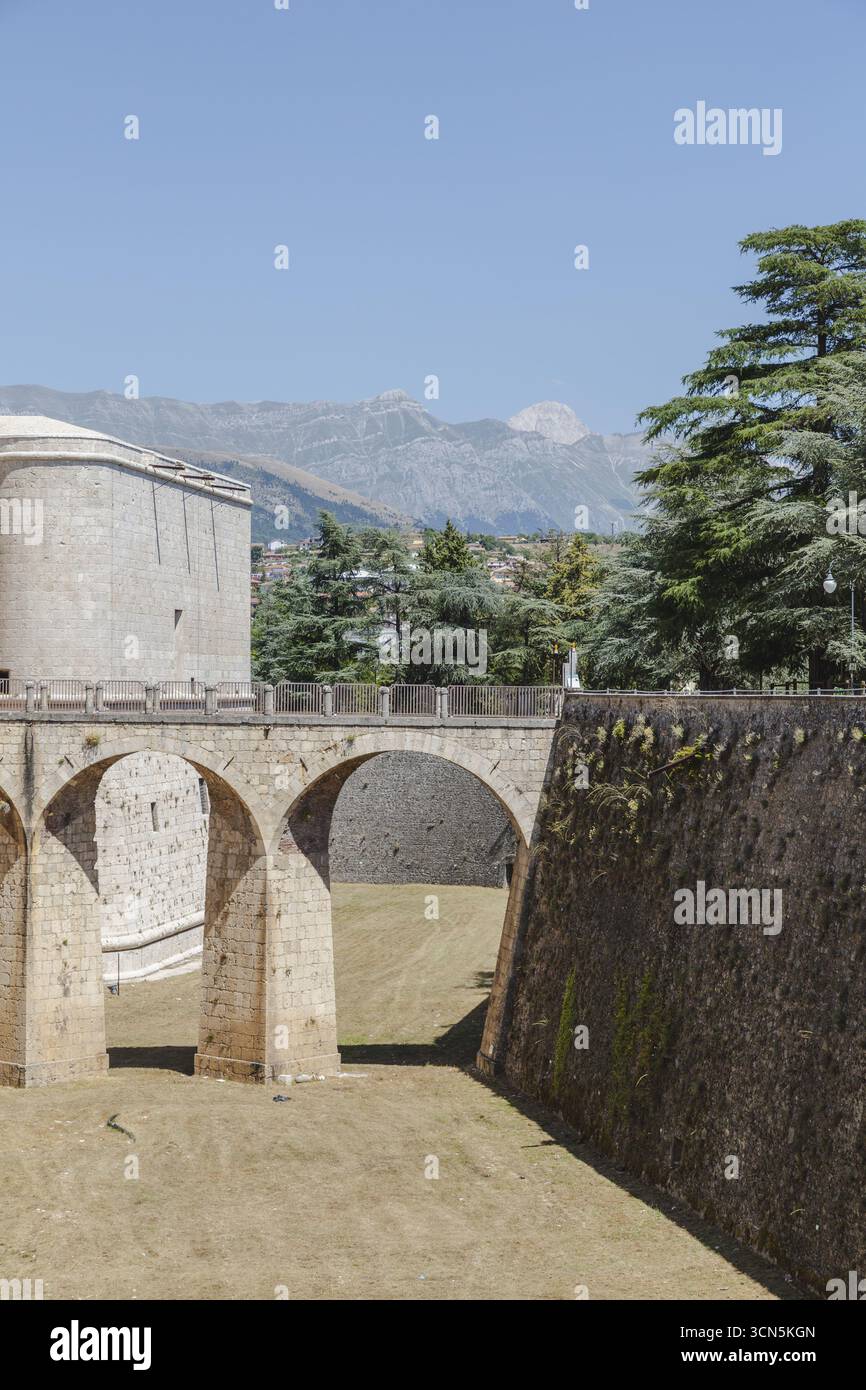 Der Blick auf alte Steinmauern und Bögen erhebt sich majestätisch vor der Kulisse ferner Berge unter klarem Himmel, eine zeitlose Szene, L'Aquila, Abruzzen, Italien. Stockfoto