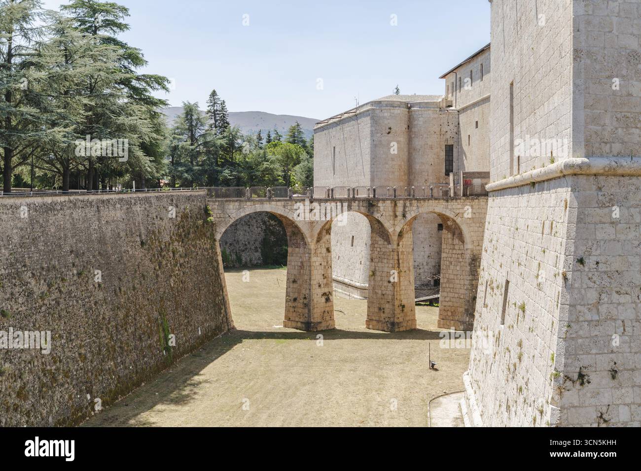 Blick auf die Festungsmauern umschließen eine Steinbrücke, die anmutig über dem trockenen Graben unter dem Sommerhimmel verläuft, L'Aquila, Abruzzen, Italien. Stockfoto