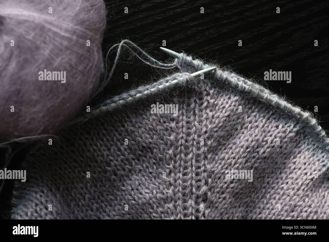 Stricken eines Pullovers auf runde Nadeln in lila Farben, Arbeit läuft Stockfoto