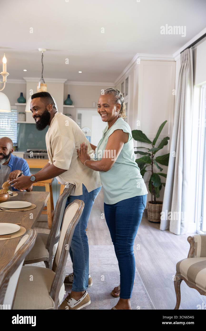 Afroamerikanische Familie bereitet in moderner Küche Mahlzeiten an einem hölzernen Esstisch mit überdachtem Gericht zu Stockfoto