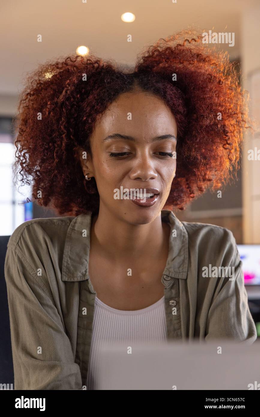 afroamerikanische Frau, die im Home Office mit Monitoren und Deckenleuchten auf einem Laptop schreibt Stockfoto