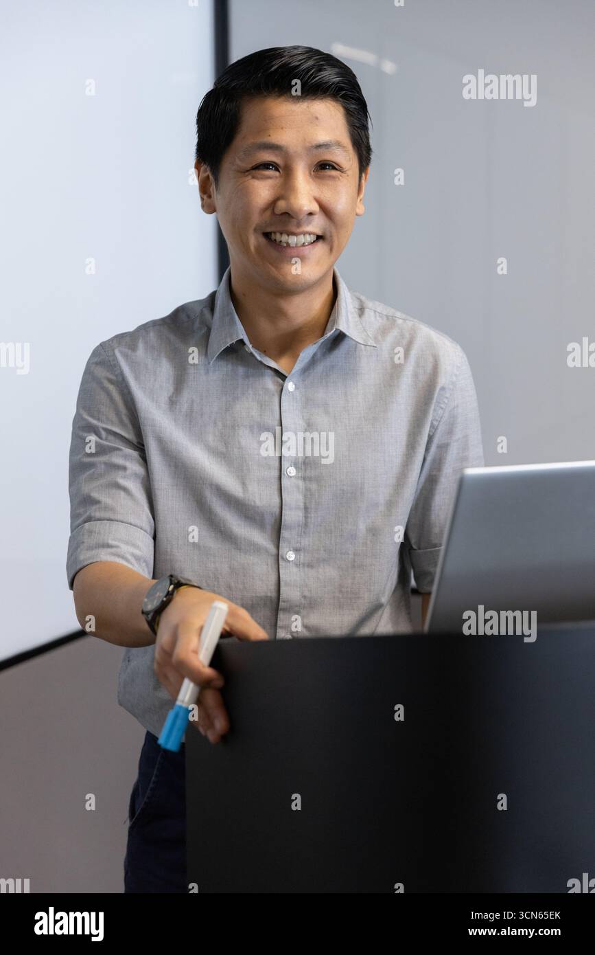 asiatischer Mann mittleren Alters, der hinter dem Podium im Konferenzraum steht, mit Markierungen und Laptop Stockfoto