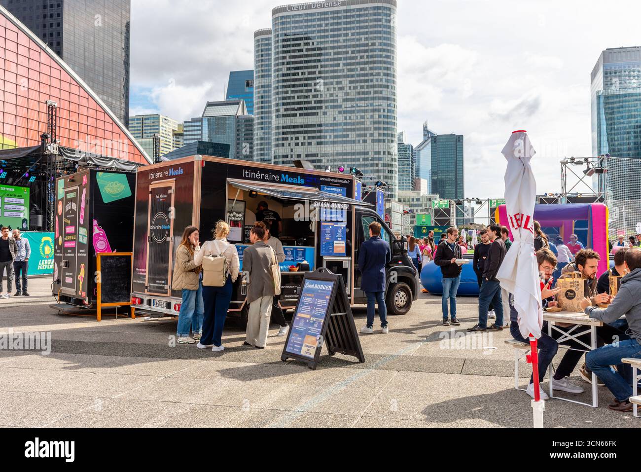 Während der Mittagszeit stehen die Leute an einem Burger Food Truck mit den Wolkenkratzern des Geschäfts- und Finanzviertels La Défense im Hintergrund Stockfoto