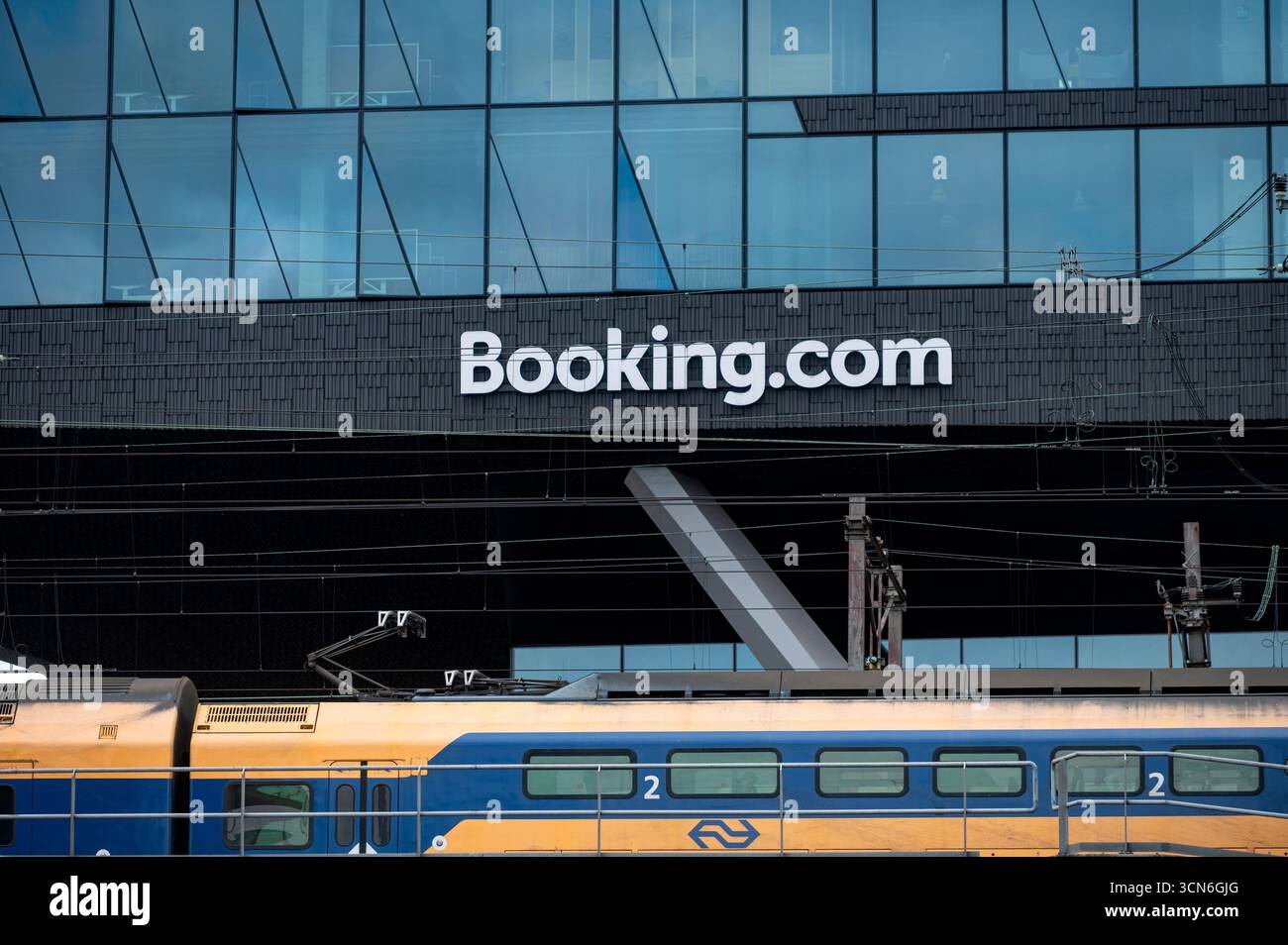Amsterdam Niederlande 23. August 2025 Booking.com Niederlassungen. Unterhalb eines Zuges der Nederlands Spoorwegen (NS) passiert. Booking.com ist ein Hotelbuch Stockfoto