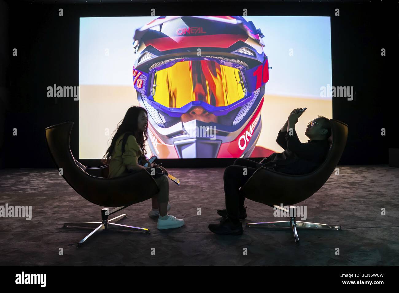 Besucher, die vor einem riesigen Fernseher sitzen, Messestand, Ausstellung, Firma Hisense, China, Chinesisch, IFA, Internationale Funkausstellung, 2025, Messe Stockfoto