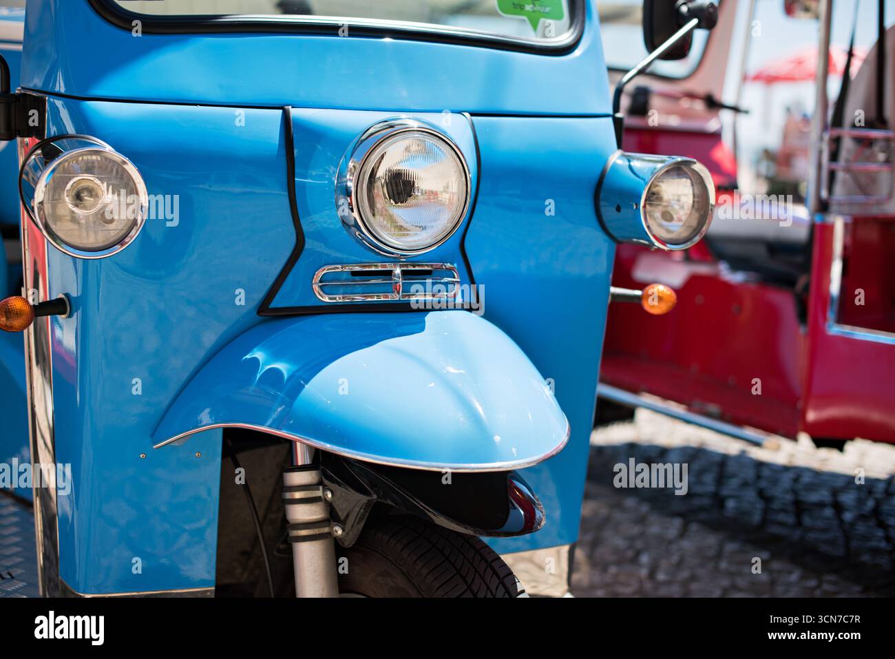 Tuk Tuk auf der Kopfsteinpflasterstraße Lissabon Portugal // LISSABON, Portugal — Ein hellblaues, dreirädriges Tuk-Tuk parkt auf einer Kopfsteinpflasterstraße in Lissabon. Diese Fahrzeuge, oft elektrisch und nach klassischen Piaggio Ape Designs angepasst, werden häufig für Führungen durch die engen, historischen Viertel der Stadt verwendet. Tuk-Tuks sind mittlerweile eine beliebte Transportmöglichkeit für Touristen, die es Besuchern ermöglicht, die steilen Hügel und engen Straßen von Gegenden wie Alfama und Bairro Alto zu erkunden. Lissabons historisches Zentrum, geprägt durch seine traditionellen Kopfsteinpflasterstraßen und farbenfrohe Architektur, stammt aus dem Jahrhundert Stockfoto