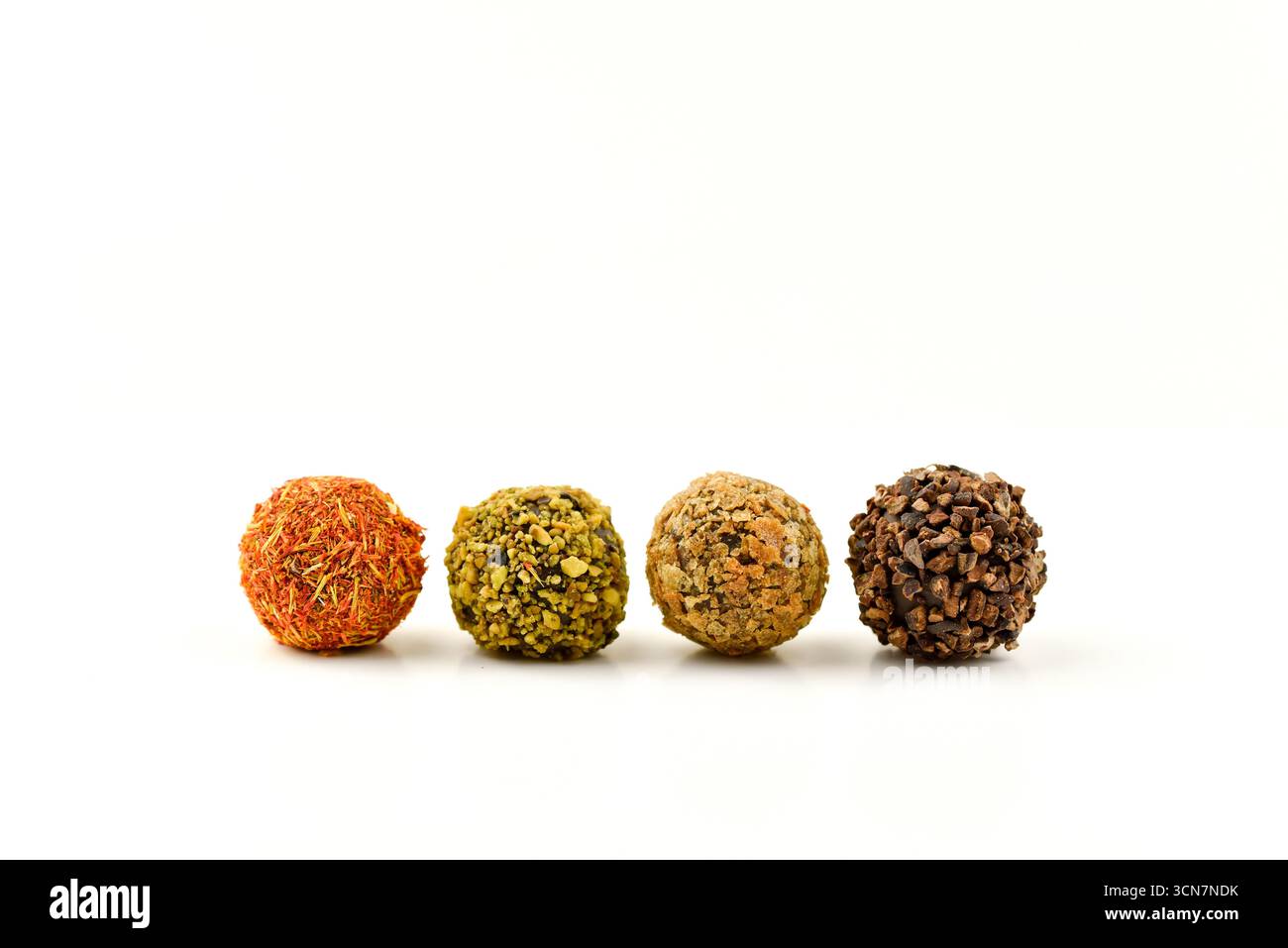 Vier unterschiedlich farbige Kugeln stehen auf weißem Hintergrund. Die Kugeln haben verschiedene Größen und Farben und scheinen aus Schokolade zu bestehen. Stockfoto