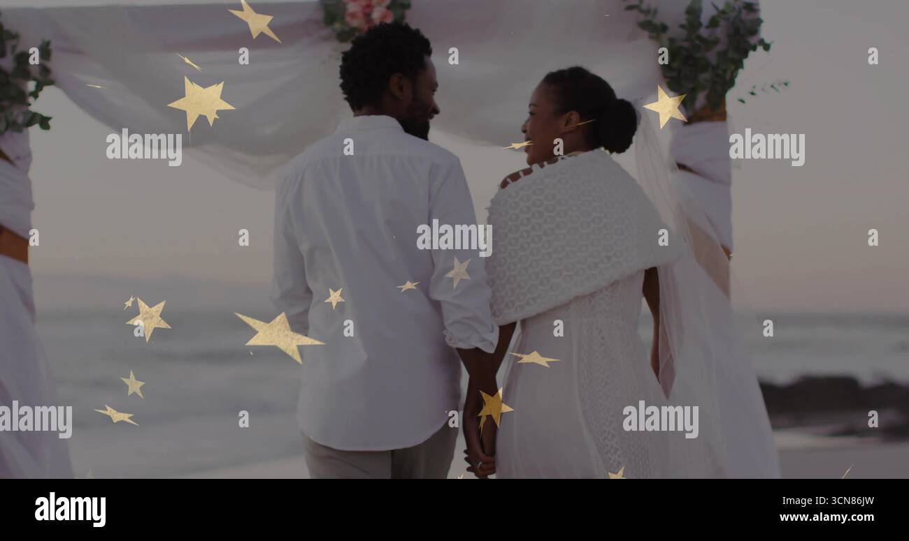 Das Ehepaar trägt Hochzeitskleidung am Strand bei Sonnenuntergang, mit drapiertem Bogen, goldenen Sternen, Wellen Stockfoto