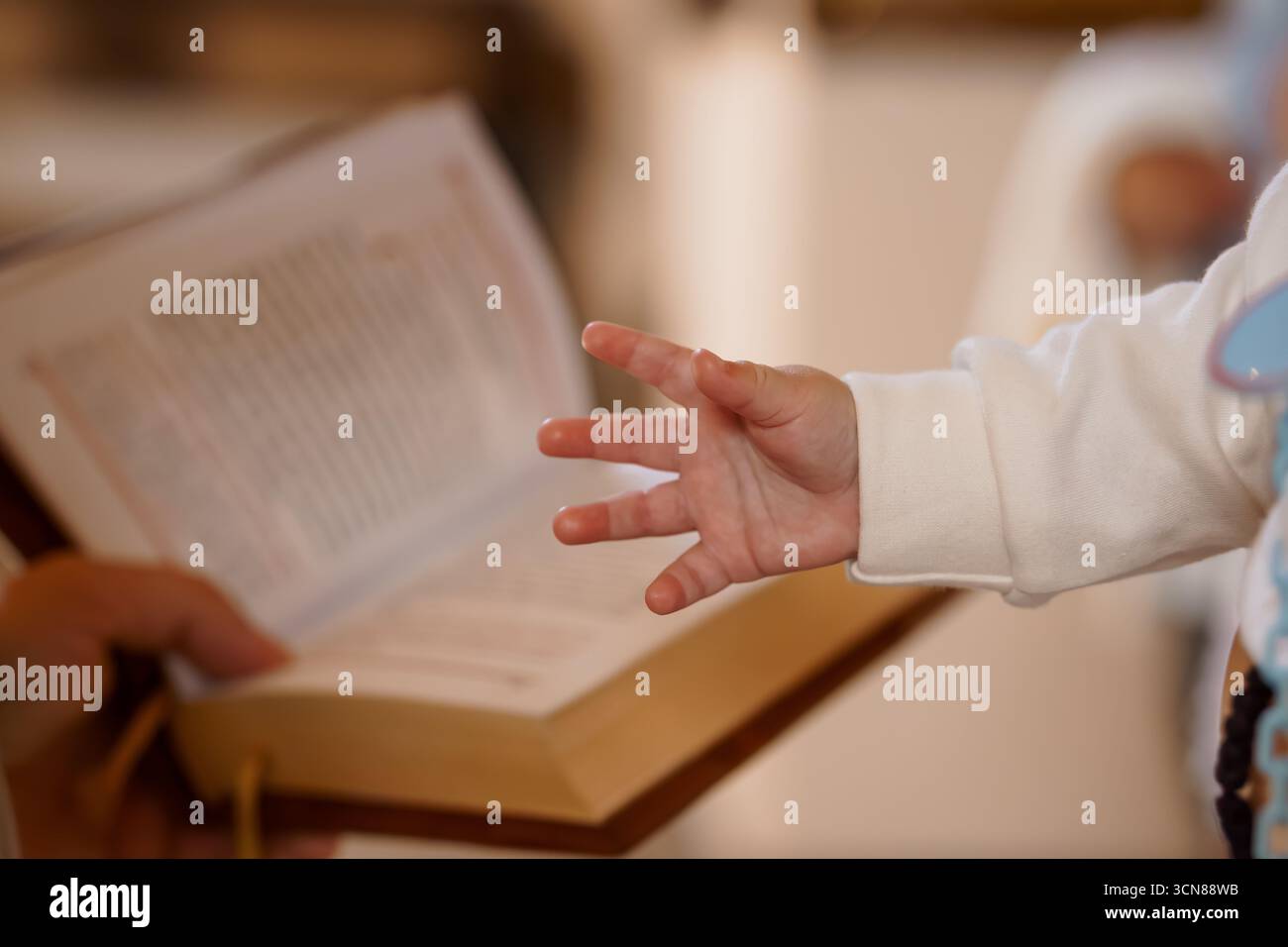 Zärtlicher Moment der Hand eines Babys, der während einer Taufe oder Taufe in Richtung einer offenen Bibel greift und glaube, Spiritualität, Hoffnung, Neuanfänge symbolisiert Stockfoto