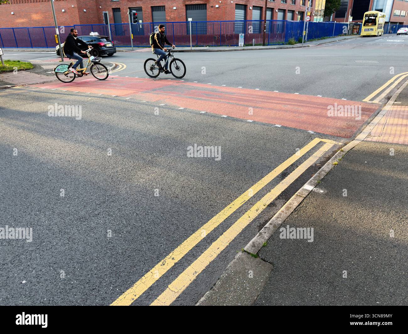 Manchester, Vereinigtes Königreich – 17. September 2025: Zwei Radfahrer überqueren eine rote Kreuzung in Manchester, um den städtischen Pendelverkehr und das Stadtleben zu erfassen. Stockfoto