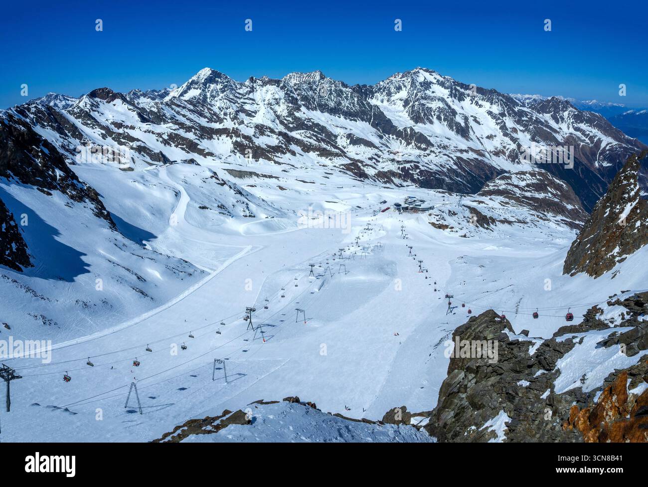 Stubaier Gletscher in den österreichischen Alpen mit Skipisten, Seilbahnbahnen, Sessellift mit Skifahrern und Snowboardern und Infrastruktur für einen Skitschlepper Stockfoto