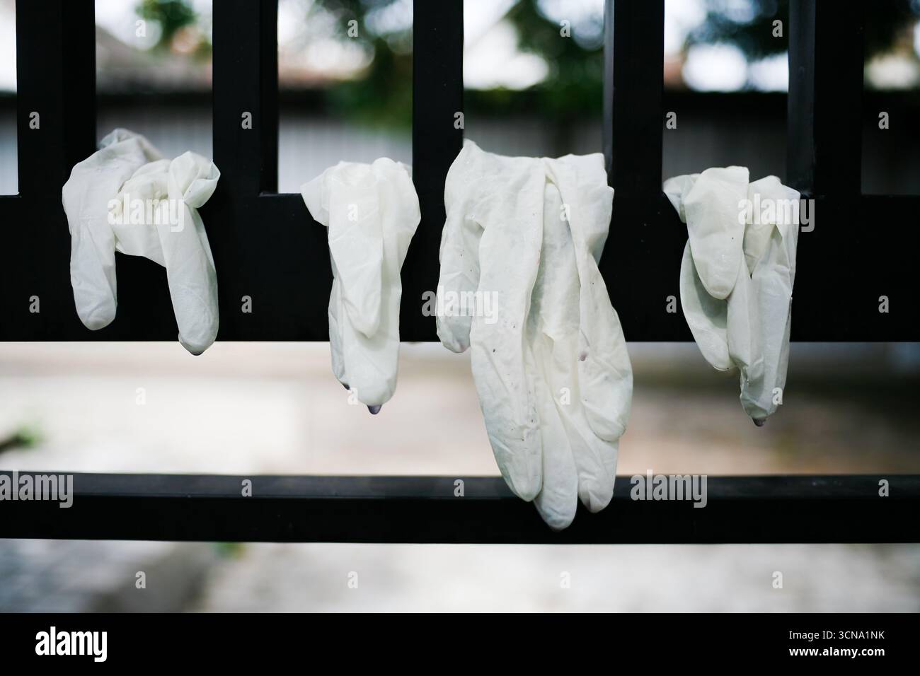Benutzte Einweghandschuhe aus Latex, die zwischen dem Eisenzaun hängen Stockfoto