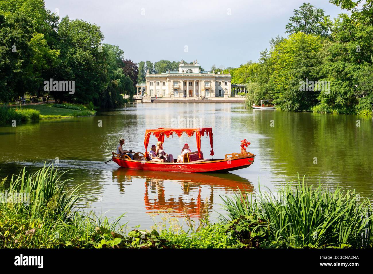 Warschau, Polen, 13.07.21. Rote Gondel mit Touristen auf dem See mit dem Palast auf der Insel (Polnisch: Palac Na Wyspie) im Hintergrund. Stockfoto