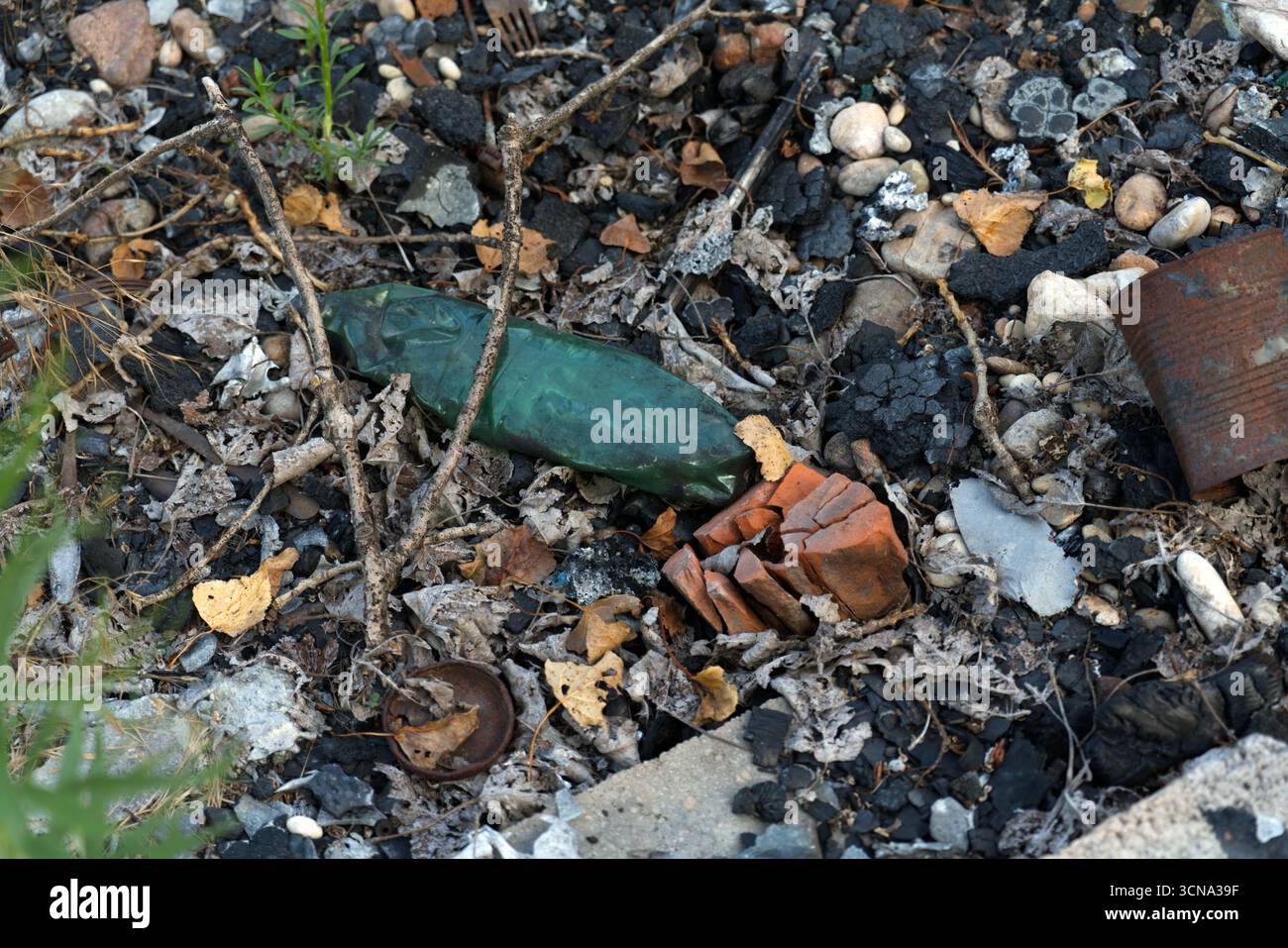 Eine grüne Glasflasche und gebrochenes Terrakotta zwischen Trümmern und verkohlten Überresten auf einem Bett aus trockenen Blättern, Felsen und Schmutz. Stockfoto