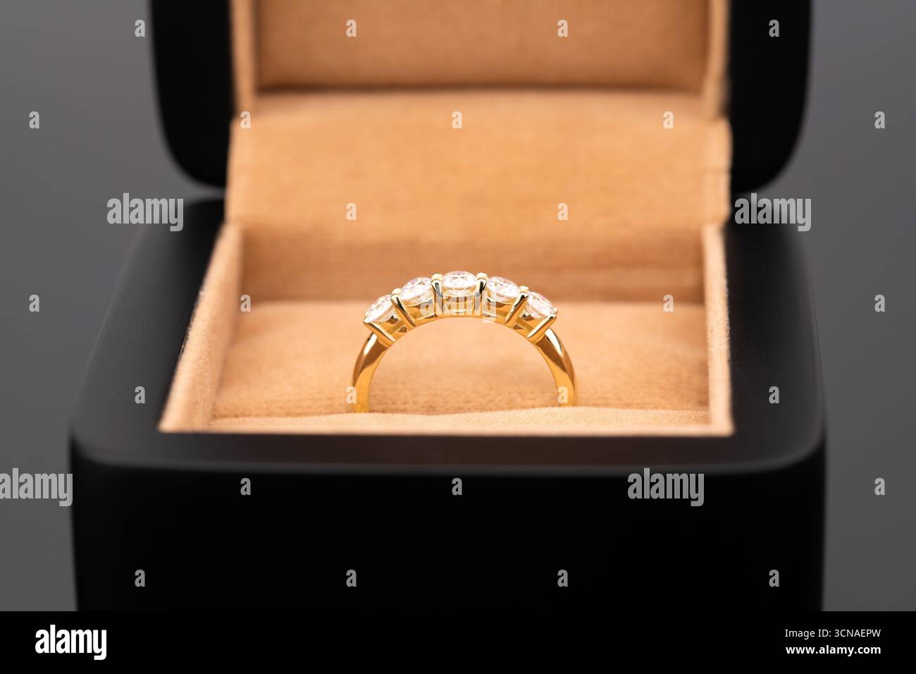 Ein goldener Ring mit Diamanten ist in einer schwarzen Box. Der Ring ist in einer goldenen Box mit einem braunen Hintergrund Stockfoto
