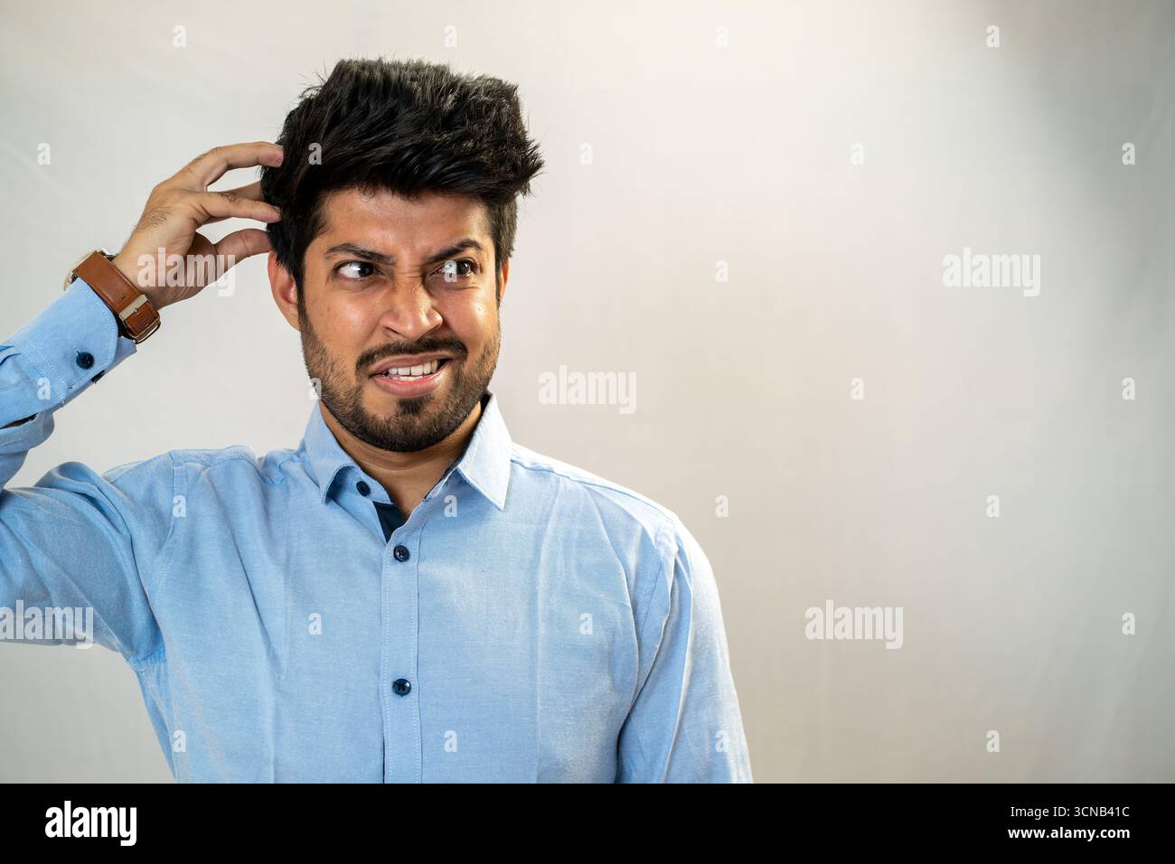 Ein junger Mann kratzt sich den Kopf mit einem verwirrten und unsicheren Ausdruck. Stockfoto