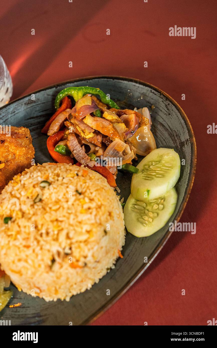 Ein großer Nahaufnahme eines Tellers asiatischer Speisen mit einer Portion gebratenem Reis, einem Rührbraten mit Fleisch und Gemüse und in Scheiben geschnittenen Gurken. Stockfoto