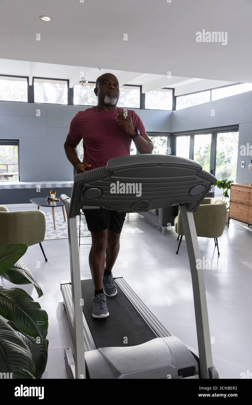 Ranghoher afroamerikaner, der Sportswear trägt, läuft auf Laufband im Wohnzimmer Stockfoto