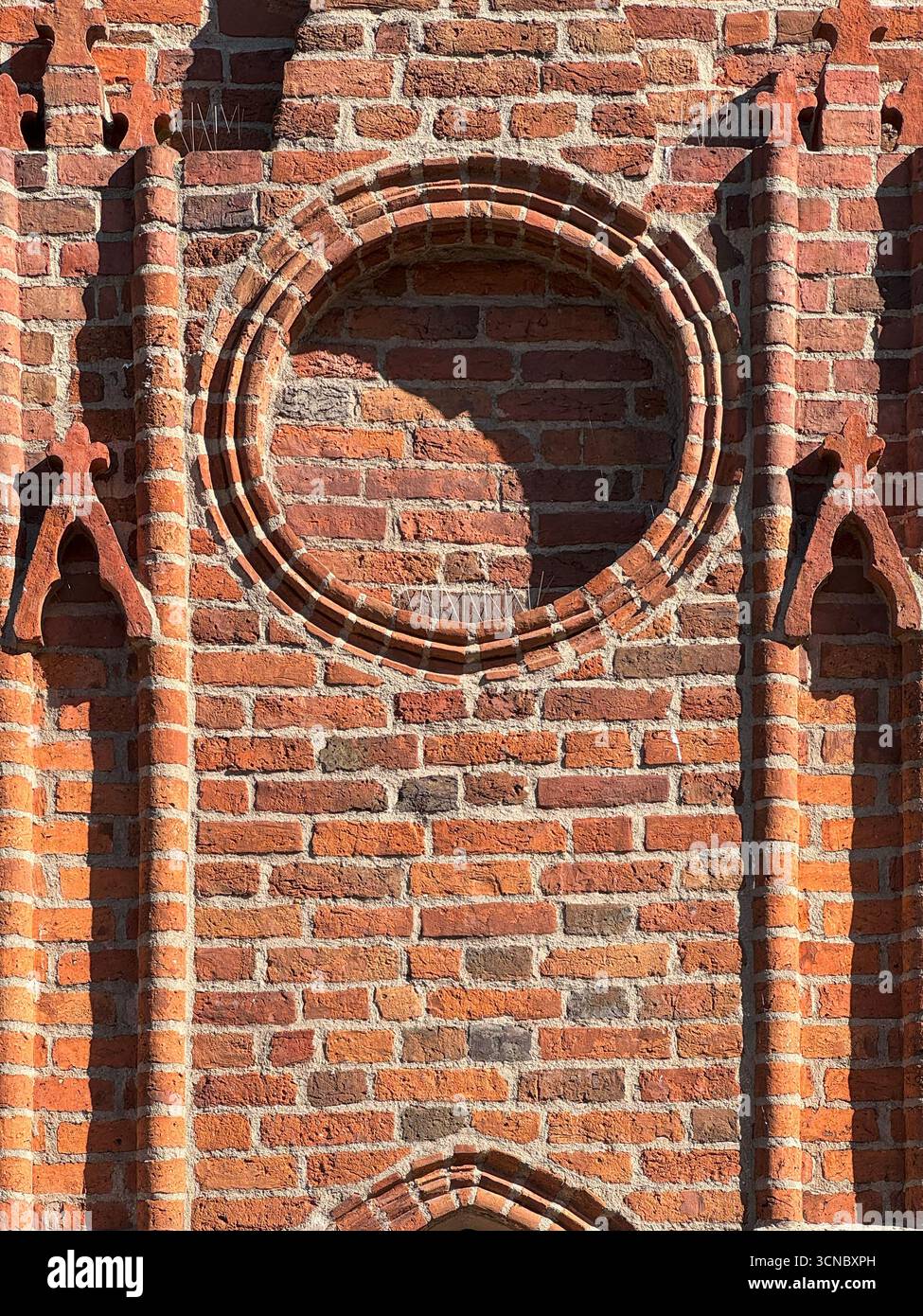 Architektonisches Detail eines runden Ziegelfensterrahmens auf gotischer Kirchenfassade, erbaut 1370 in Europa. Ein Merkmal mittelalterlicher Handwerkskunst und katholisch Stockfoto