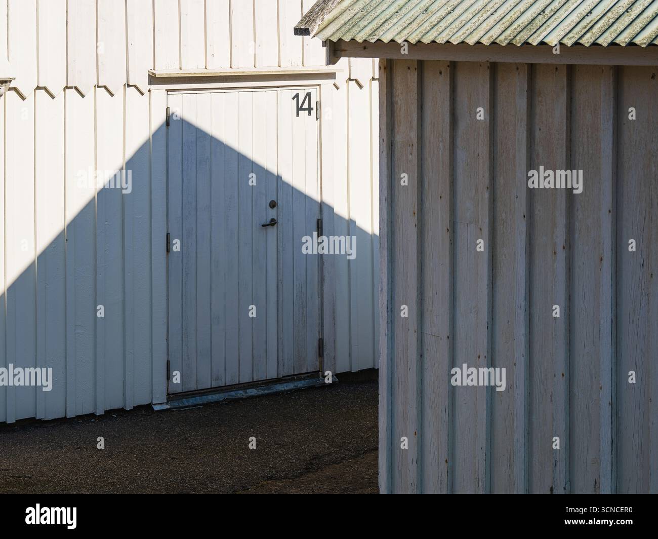 Zwei weiße Holzkonstruktionen stehen vor einem klaren Himmel und zeigen eine Tür mit der Zahl 14. Die Sonne wirft einen Schatten und fügt der Szene einen Kontrast hinzu. Stockfoto