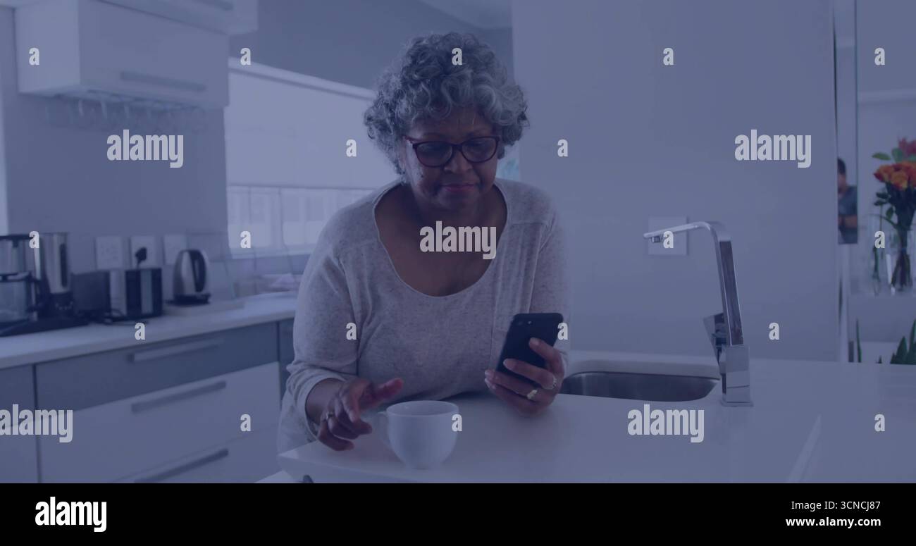 Smartphone in der Hand, Seniorin berührt Kaffeetasse auf der modernen Kücheninsel, mit orangefarbenen Blumen Stockfoto