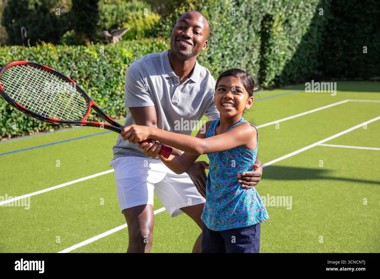Vielseitige Vater und Tochter üben Tennisschaukel auf dem Tennisplatz mit rot-schwarzem Schläger Stockfoto
